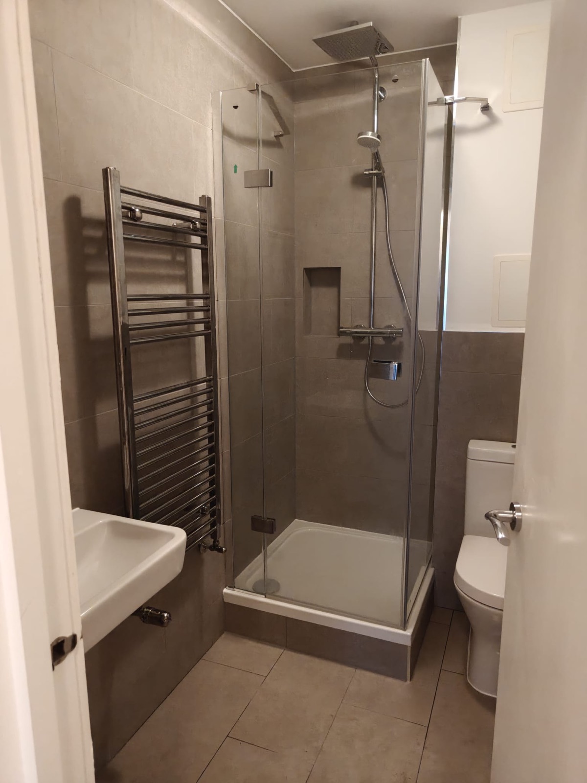 Renovated shower room with a frameless glass enclosure, rainfall shower, tiled niche, towel radiator, basin and WC, Shepherd's Bush W12